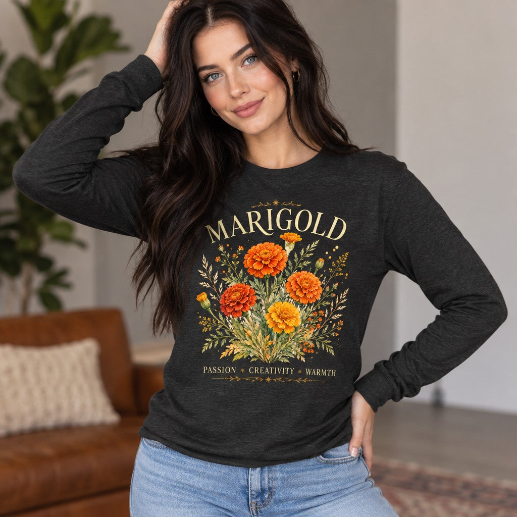Woman wearing a dark grey heather Bella Canvas® 3501 long sleeve with a vintage watercolor marigold bouquet design, featuring gold and orange blooms under 'MARIGOLD' in elegant serif font and floral-trimmed lines, autumnal flower symbolism, cozy living room setting, perfect for October birthdays, gardeners, and floral lovers, by Crossroads Dandelion
