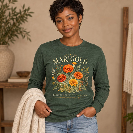 Woman in a heather forest Bella Canvas® long sleeve shirt featuring a lush watercolor gold and orange marigold bouquet with elegant serif text, vintage botanical style, cozy indoor scene, for October birthdays, gardeners, and floral lovers, by Crossroads Dandelion