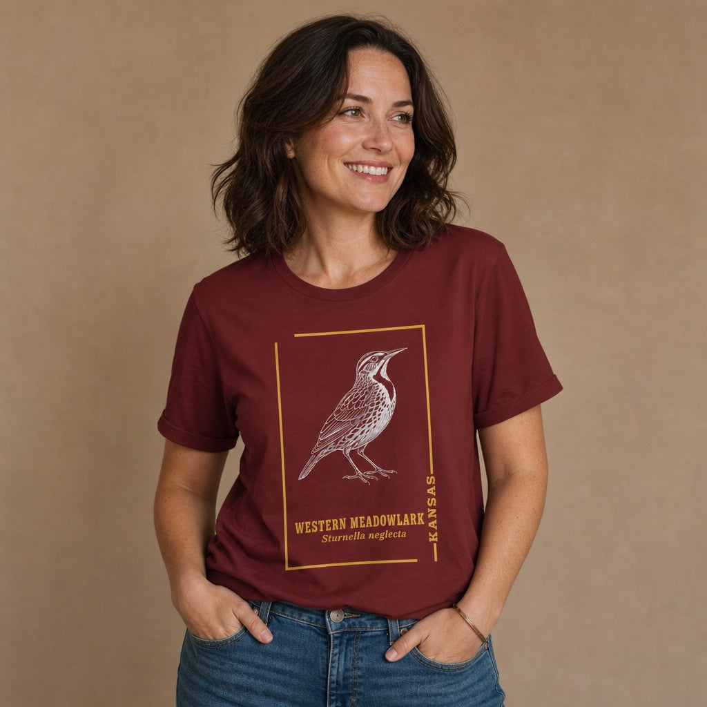 Woman wearing a cardinal red Bella Canvas 3001 t-shirt featuring a vintage black-and-white meadowlark illustration within a golden botanical frame and classic serif text, inspired by antique field guides, for bird lovers and prairie nostalgia enthusiasts, by Crossroads Dandelion