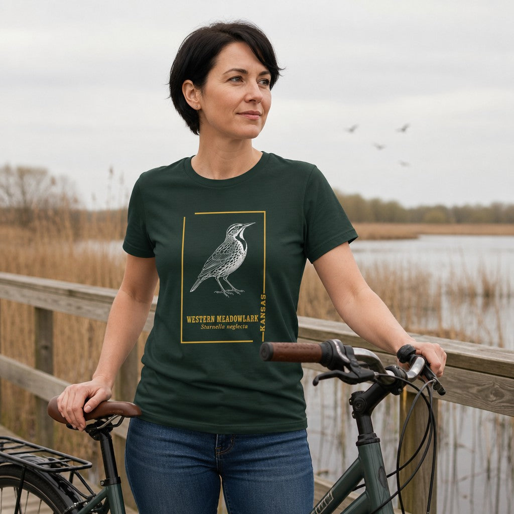 Woman in forest green Bella Canvas 3001 t-shirt featuring a vintage black-and-white meadowlark line art design with golden botanical frame and scientific name, standing by a lakeside boardwalk, perfect for bird lovers and prairie nostalgia fans, by Crossroads Dandelion
