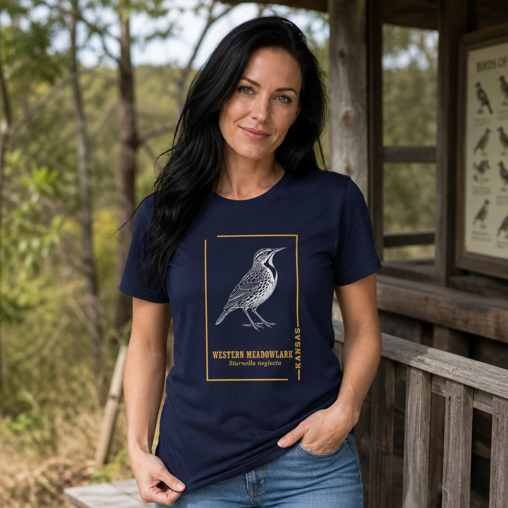 Woman wearing a navy Bella Canvas 3001 t-shirt with a vintage black-and-white meadowlark illustration framed in gold, classic serif typography and scientific name, rustic cabin porch setting, ideal for bird lovers and prairie nostalgia enthusiasts, by Crossroads Dandelion