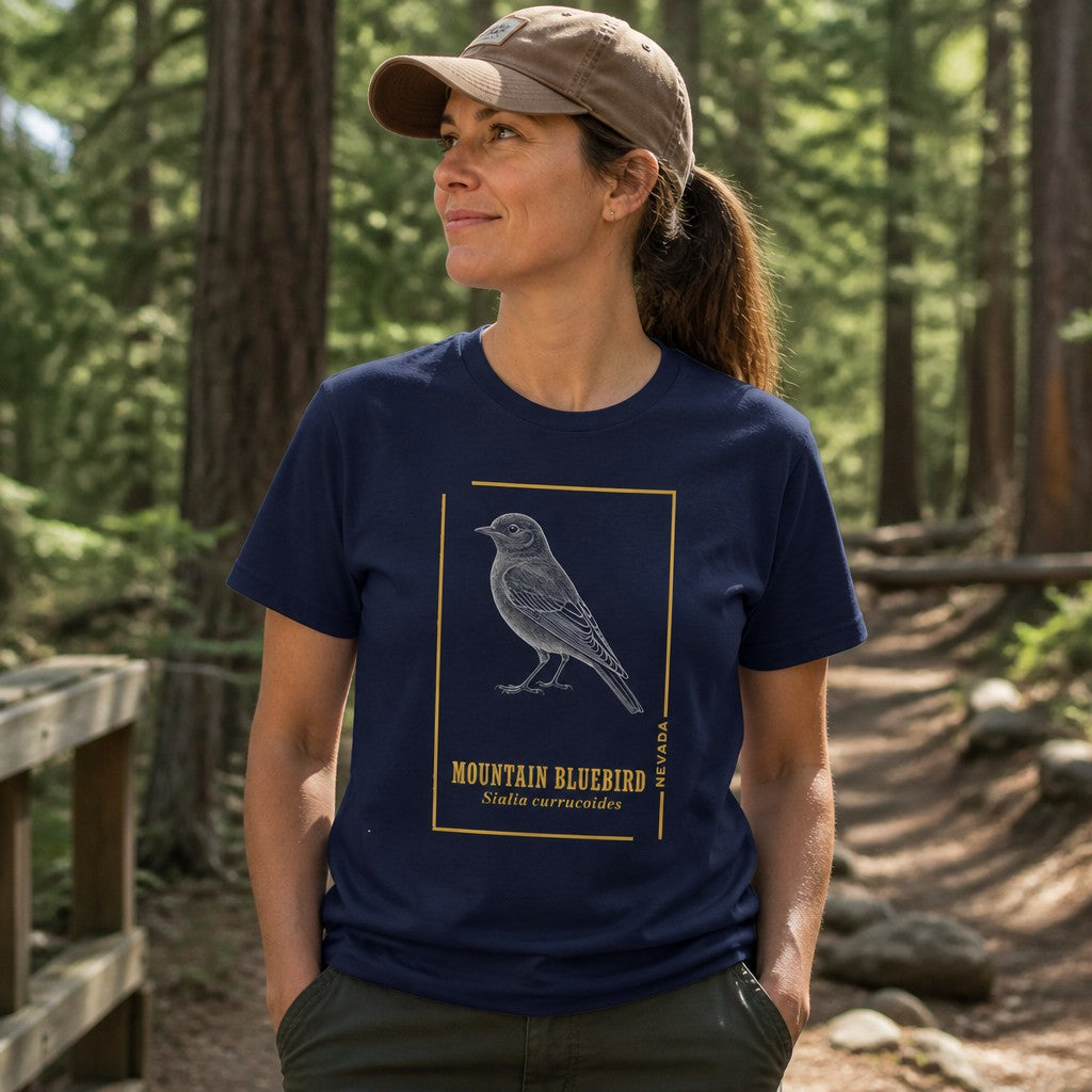 Woman wearing a navy Bella Canvas 3001 t-shirt with a vintage etched mountain bluebird illustration framed in gold accents, standing on a forest trail, ideal for bird watchers, naturalists, and cottagecore lovers, by Crossroads Dandelion
