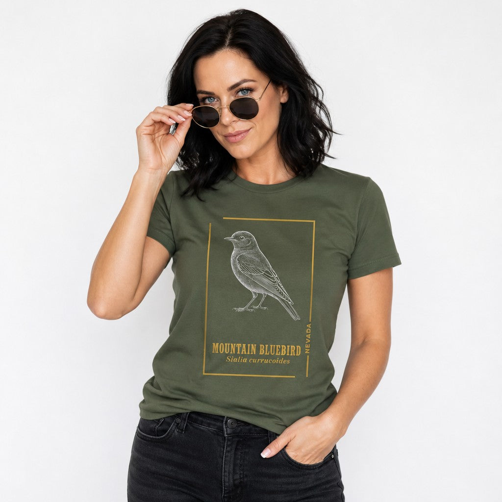 Woman wearing a military green Bella Canvas 3001 t-shirt with a vintage-style etched illustration of a mountain bluebird framed in gold accents, field guide aesthetic, perfect for birders and cottagecore fans, by Crossroads Dandelion