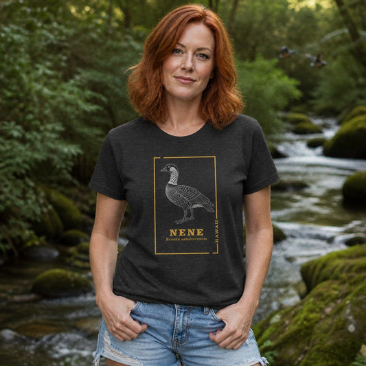 Woman in dark grey heather Bella Canvas 3001 t-shirt featuring a vintage line art illustration of a nene goose framed by golden botanical borders, celebrating Hawaii's rare state bird for birdwatchers and nature lovers, outdoors by a forest river, by Crossroads Dandelion