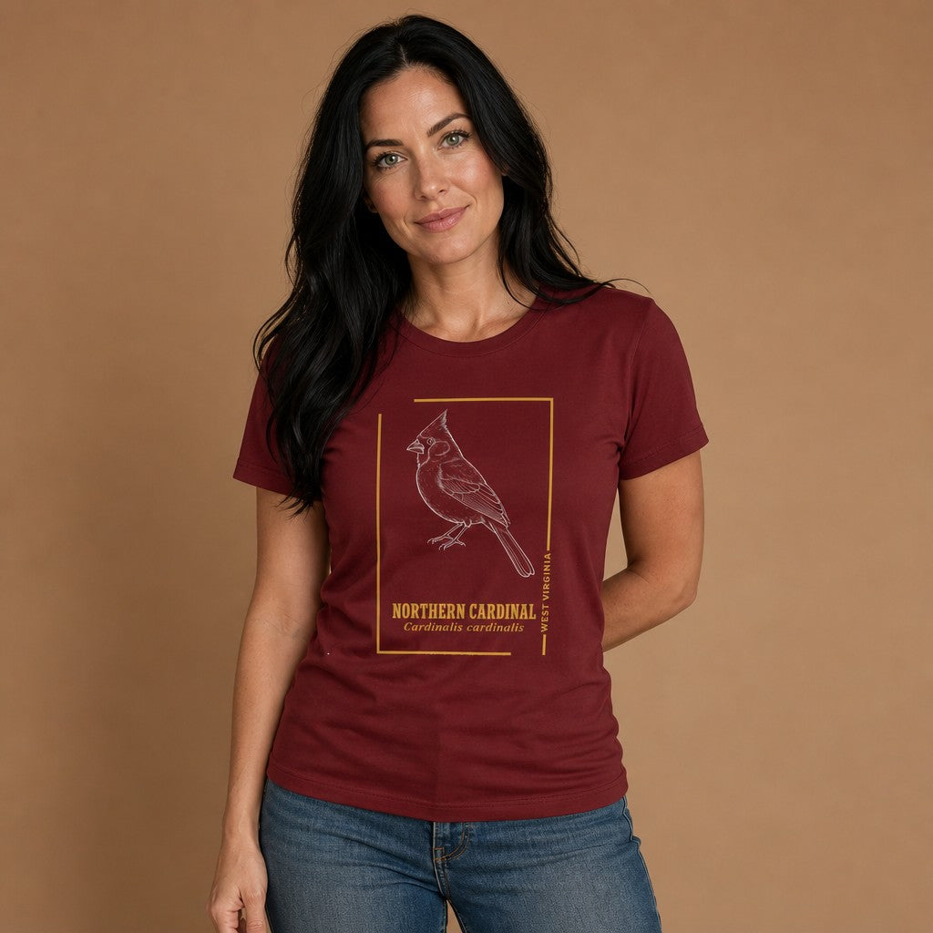 Woman wearing a cardinal red Bella Canvas 3001 t-shirt featuring a vintage-style hand-drawn Northern Cardinal illustration in a golden border with Latin name and state designation, vintage botanical line art for birdwatchers and nature lovers, by Crossroads Dandelion