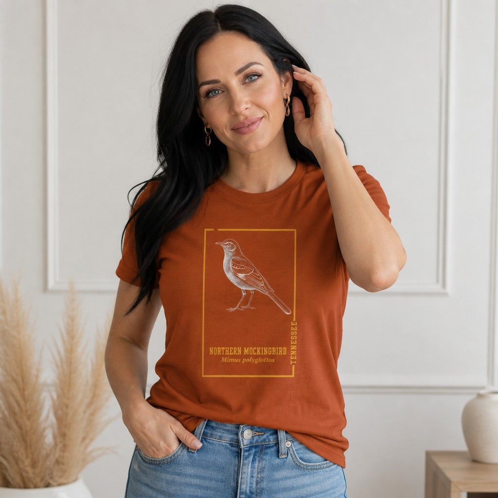 Woman in autumn rust Bella Canvas 3001 t-shirt featuring a vintage-style engraved northern mockingbird design inside a golden botanical frame, antique field guide inspired, ideal for birdwatchers and Appalachian wildlife lovers, by Crossroads Dandelion