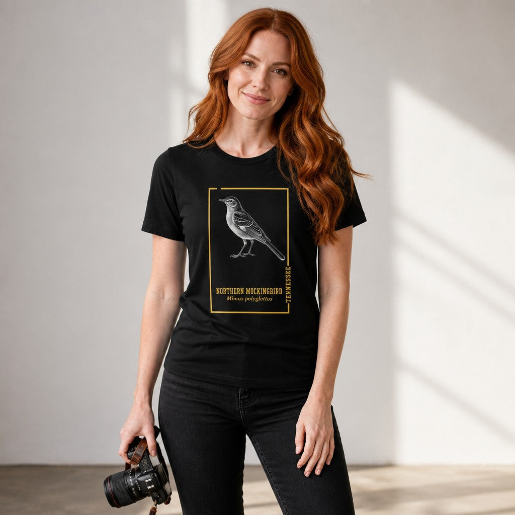Woman in black Bella Canvas 3001 t-shirt featuring a vintage-style northern mockingbird engraving inside a golden botanical frame, inspired by antique field guides, ideal gift for birdwatchers and Appalachian wildlife lovers, photographed in a bright indoor studio, by Crossroads Dandelion