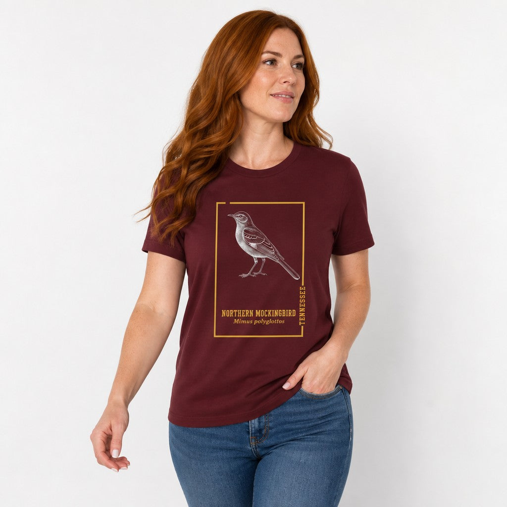 Woman wearing a maroon Bella Canvas 3001 t-shirt featuring a vintage-style northern mockingbird engraving inside a golden botanical frame, inspired by antique field guides, perfect for birdwatchers and Appalachian wildlife lovers, by Crossroads Dandelion