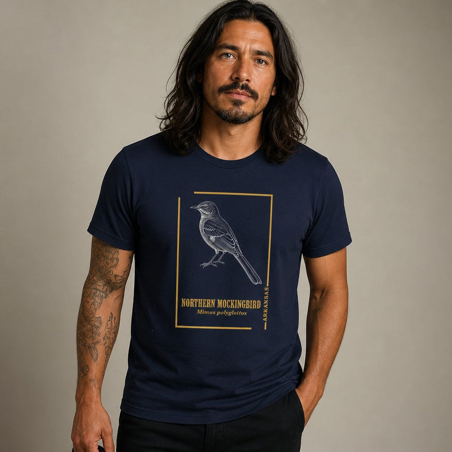 Man wearing a navy Bella Canvas 3001 t-shirt with a vintage hand-drawn Northern Mockingbird illustration framed in gold, evoking classic field guide art, ideal for birdwatchers, nature enthusiasts, and lovers of southern woodlands, by Crossroads Dandelion