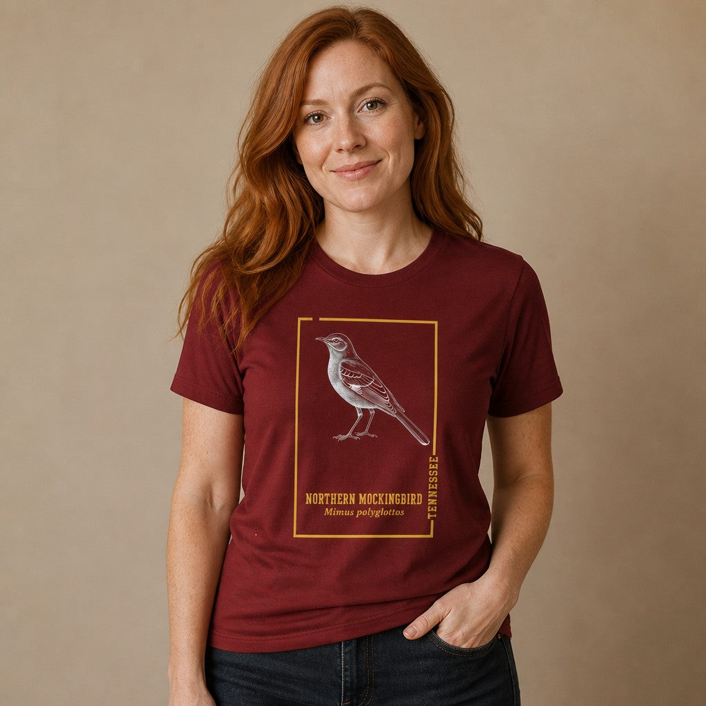 Woman wearing a cardinal red Bella Canvas 3001 t-shirt featuring a vintage-style northern mockingbird engraving within a golden botanical frame, inspired by antique field guides, perfect for birdwatchers and nature illustration lovers, by Crossroads Dandelion
