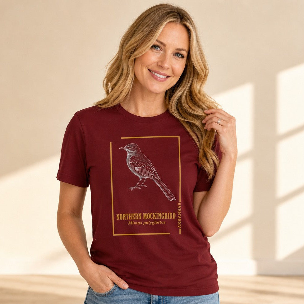 Woman in cardinal red Bella Canvas 3001 t-shirt featuring a vintage-style hand-rendered Northern Mockingbird illustration with a gold border, inspired by antique field guides, perfect for birdwatchers and nature lovers, indoor casual scene, by Crossroads Dandelion
