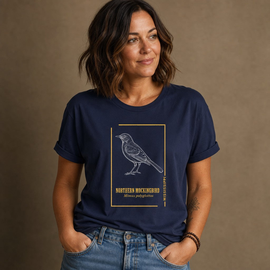Woman wearing a navy Bella Canvas 3001 t-shirt featuring a vintage hand-sketched Northern Mockingbird illustration with gold botanical accents, naturalist style, for birdwatchers and classic wildlife art lovers, by Crossroads Dandelion