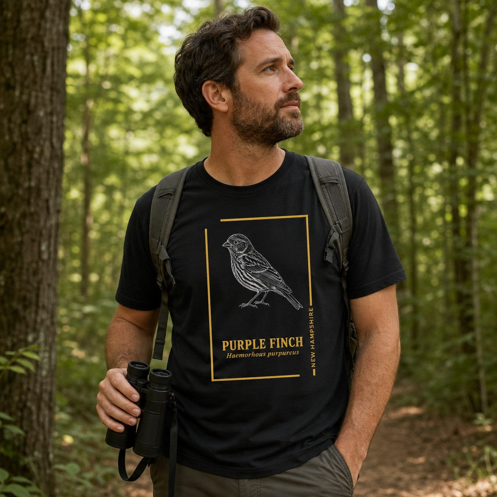 Man wearing a black Bella Canvas 3001 t-shirt with a vintage-inspired hand-illustrated Purple Finch design framed in gold, botanical field guide style, hiking in a lush green forest, perfect for wildlife lovers, birdwatchers, and New England nostalgia, by Crossroads Dandelion