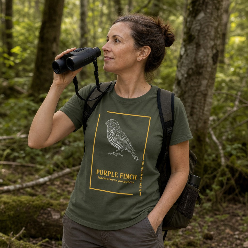 Woman wearing a military green Bella Canvas 3001 t-shirt featuring a vintage-inspired, hand-illustrated Purple Finch in white ink with gold frame and serif typography, perfect for wildlife and forest lovers, hiking in the woods, by Crossroads Dandelion