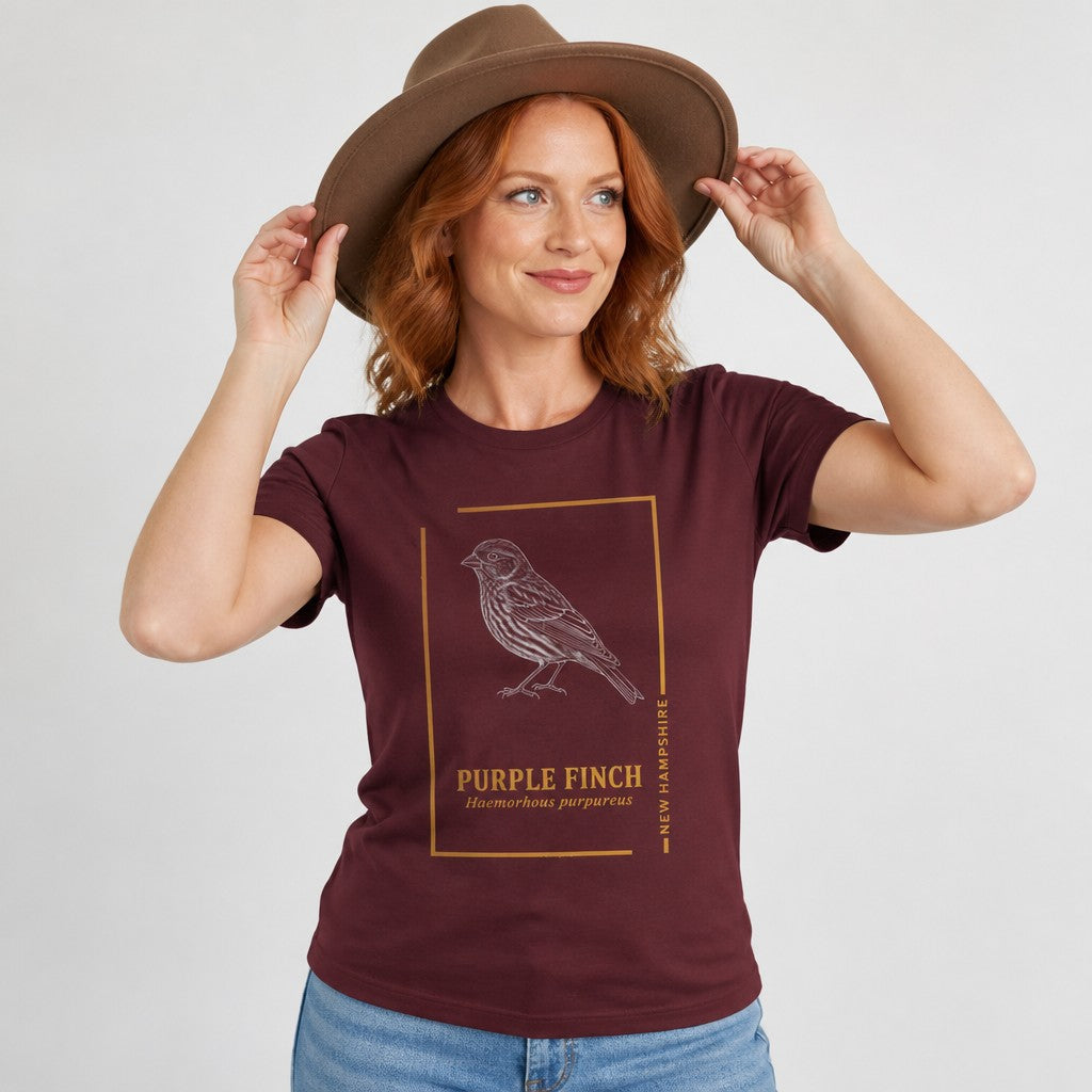 Woman wearing a maroon Bella Canvas 3001 t-shirt featuring a vintage hand-illustrated Purple Finch and elegant field guide typography in a gold frame, perfect for wildlife lovers and New England nostalgia fans, by Crossroads Dandelion