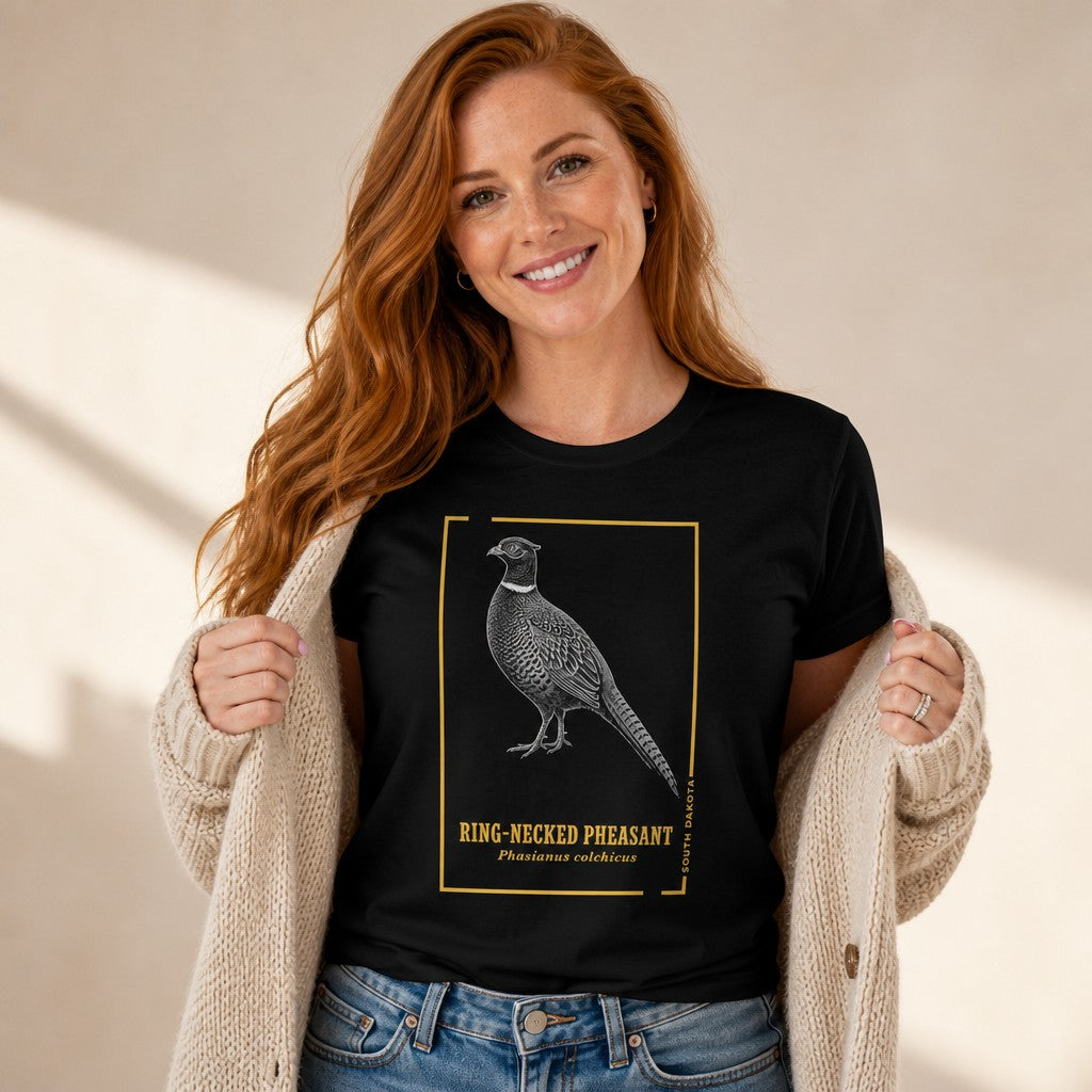 Smiling woman wearing a black Bella Canvas 3001 t-shirt with a hand-illustrated vintage ring-necked pheasant design, classic engraving style with golden frame and lettering, cozy indoor scene, birdwatchers and nature lovers, by Crossroads Dandelion