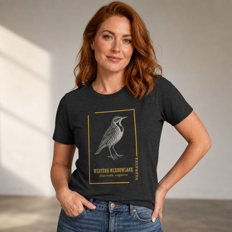 Woman wearing a dark grey heather Bella Canvas 3001 t-shirt with a vintage hand-drawn Western Meadowlark wildlife illustration framed in golden accents, classic field guide design for birders and nature lovers, by Crossroads Dandelion