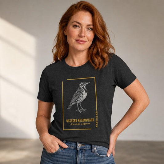 Woman wearing a dark grey heather Bella Canvas 3001 t-shirt with a vintage hand-drawn Western Meadowlark wildlife illustration framed in golden accents, classic field guide design for birders and nature lovers, by Crossroads Dandelion
