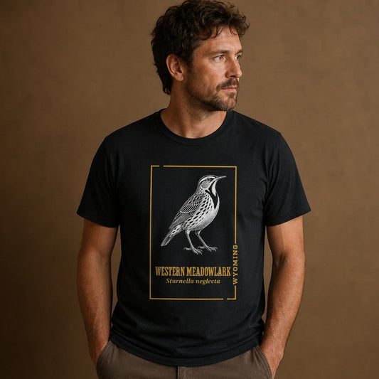 Man wearing black Bella Canvas 3001 t-shirt with a vintage hand-inked illustration of the Western Meadowlark framed in gold, detailed nature journal style for birdwatchers and Wyoming lovers, casual indoor portrait, by Crossroads Dandelion