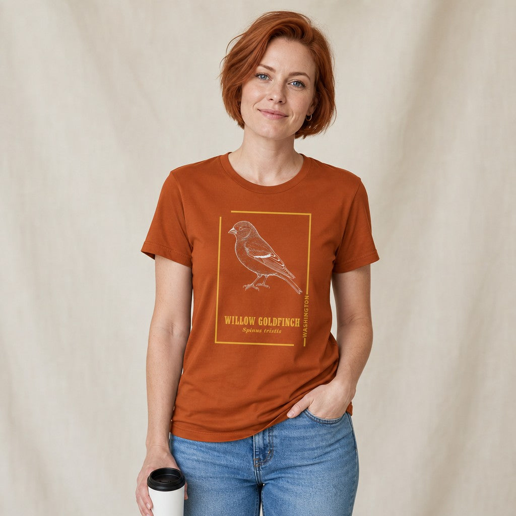 Red-haired woman in autumn Bella Canvas 3001 t-shirt featuring a vintage etching style willow goldfinch framed in gold, inspired by classic field journal sketches, boutique botanical art gift for birdwatchers and nature lovers, by Crossroads Dandelion