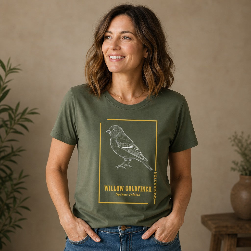Woman wearing a military green Bella Canvas 3001 t-shirt with a vintage etching style willow goldfinch design, golden accents, classic serif text, in a cozy indoor botanical setting, nature lovers and birdwatchers apparel, by Crossroads Dandelion