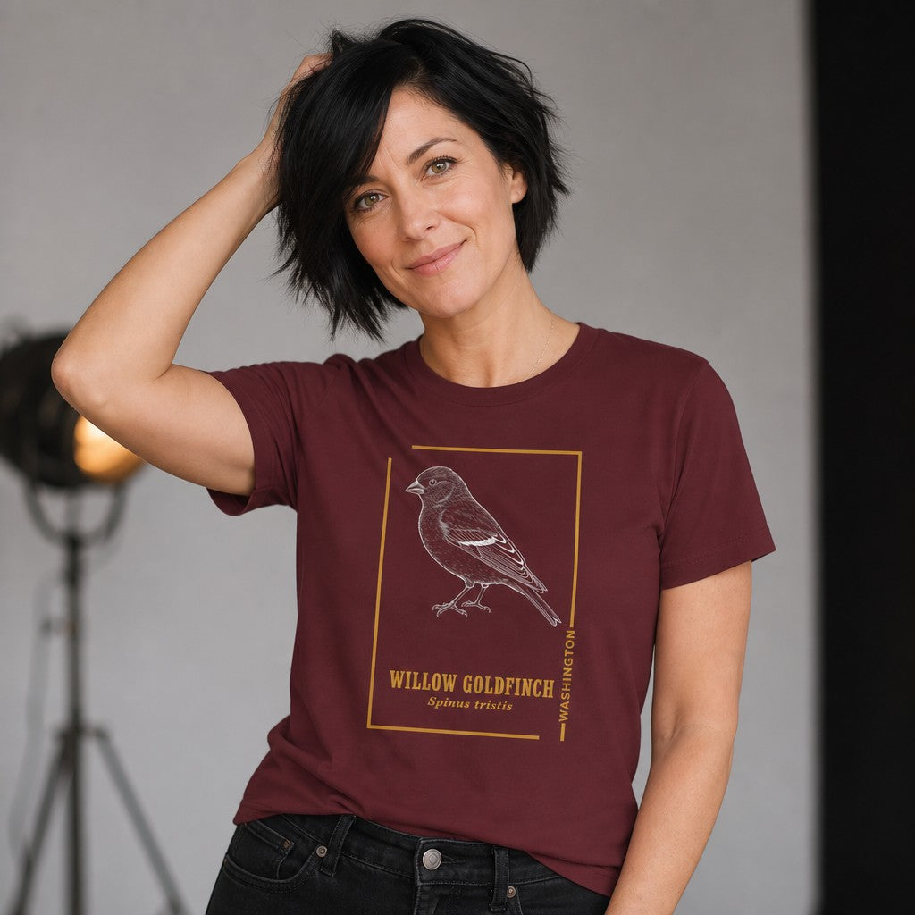 Woman wearing a maroon Bella Canvas 3001 t-shirt with a vintage etching style willow goldfinch design framed in gold, inspired by nature field journal sketches, studio setting, ideal for birdwatchers and botanical art lovers, by Crossroads Dandelion