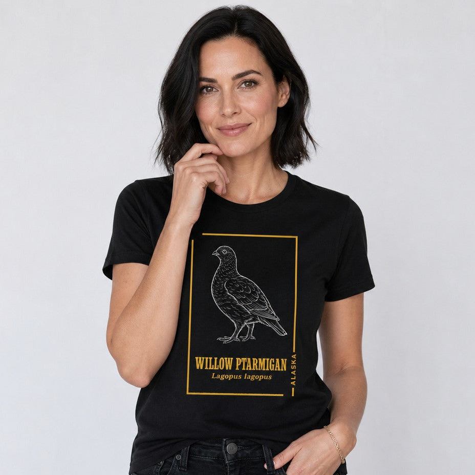 Woman wearing a black Bella Canvas 3001 t-shirt featuring a vintage-style hand-drawn illustration of the willow ptarmigan, Alaska state bird, framed with golden botanical accents, nostalgic naturalist field journal design, perfect for birdwatchers, wildlife and cottagecore lovers, by Crossroads Dandelion