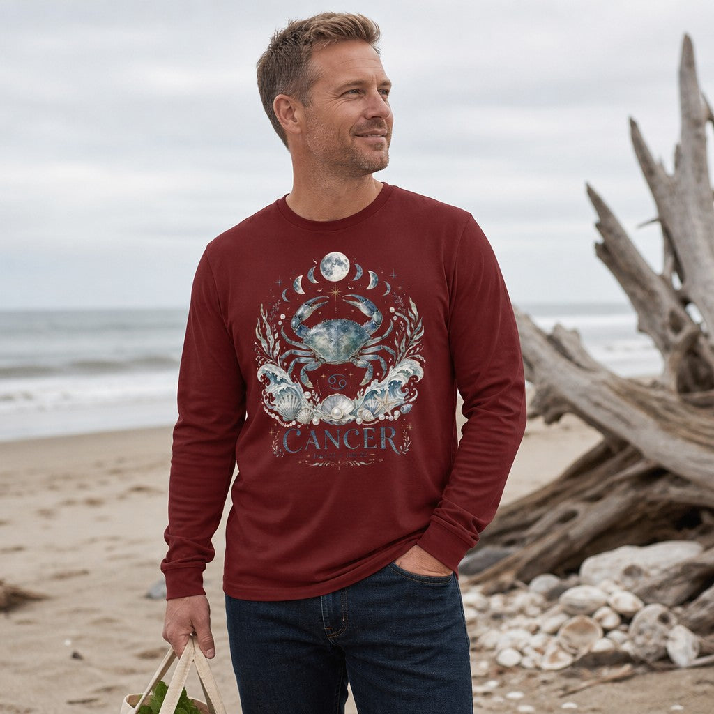 Man in cardinal red Bella Canvas 3501 long sleeve featuring a watercolor celestial crab with ocean waves, seashells, pearls, moon phases, and Cancer zodiac symbolism, standing on a driftwood-strewn beach, astrology and nature lovers apparel, by Crossroads Dandelion