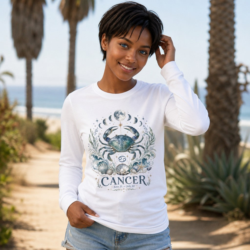 Woman wearing a white Bella Canvas 3501 long sleeve with a watercolor celestial crab Cancer zodiac design, adorned with ocean waves, shells, pearls, moon phases, and botanical accents, standing on a sunny beach path with palm trees, for astrology and nature lovers, by Crossroads Dandelion