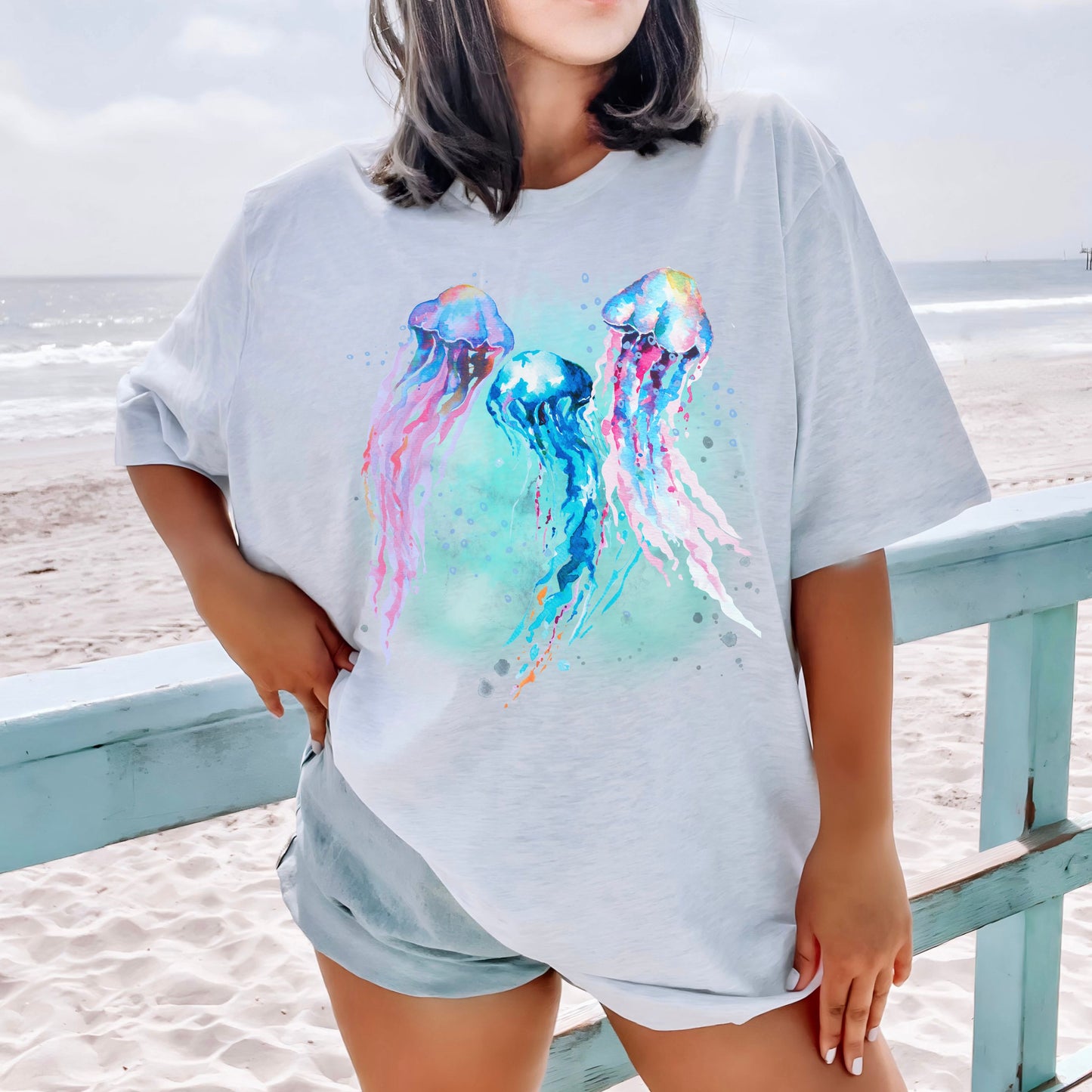 Person wearing a light gray (ash) t-shirt with colorful jellyfish design on a beach
