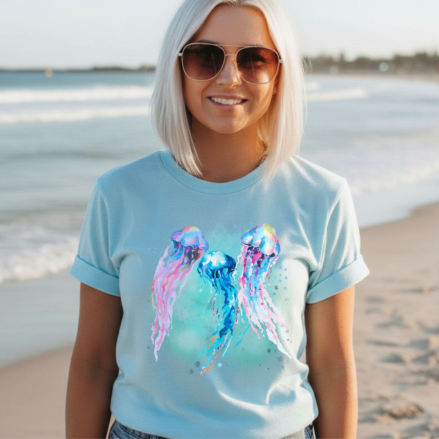 Woman wearing an ice blue t-shirt with colorful jellyfish design on a beach.