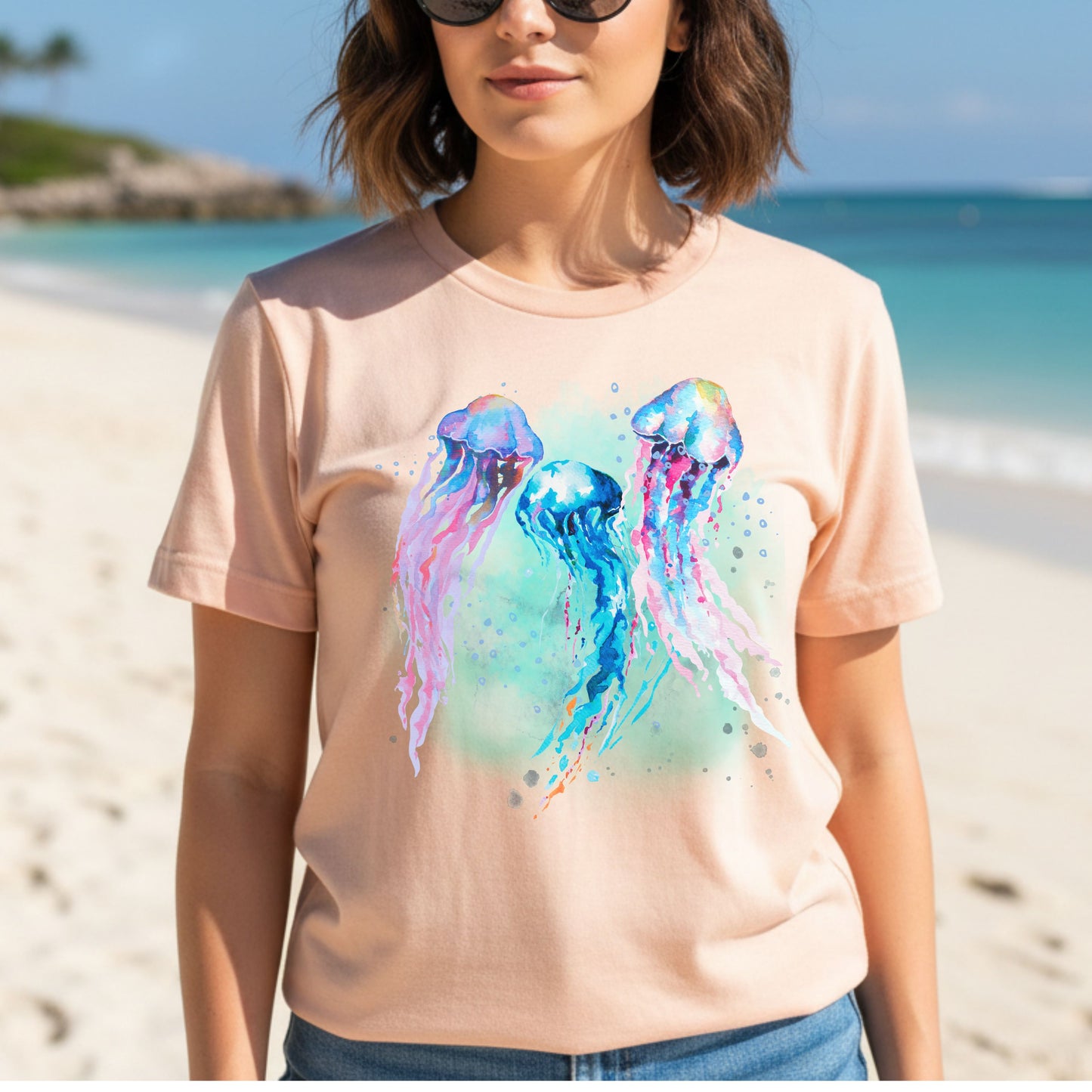 Lady wearing a heather peach t-shirt with a colorful jellyfish design on a beach.