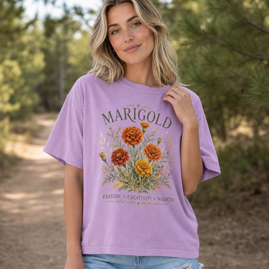 Woman wearing an orchid Comfort Colors 1717 t-shirt with a watercolor marigold bouquet design, intricate botanical details, warm and vibrant for artists and gardeners, photographed on a forest path, for women and flower lovers, by Crossroads Dandelion