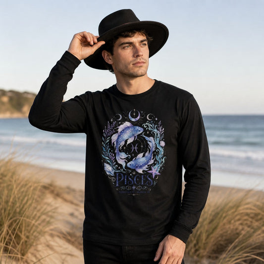 Man wearing a black Bella Canvas 3501 long sleeve with a watercolor Pisces design featuring luminous koi fish, celestial moons, and violet florals, standing on a coastal beach, astrology lovers, by Crossroads Dandelion