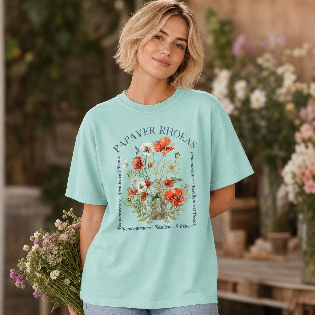 Woman in chalky mint Comfort Colors 1717 t-shirt featuring a hand-drawn watercolor poppy floral design with elegant script, standing in a greenhouse holding wildflowers, cottagecore style for nature and flower lovers, by Crossroads Dandelion