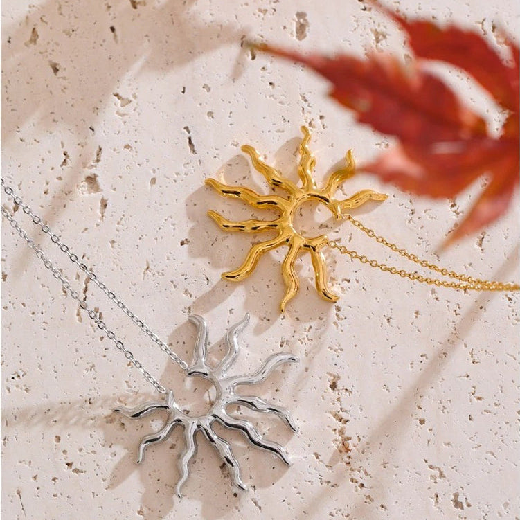Gold and silver wavy sun pendant necklaces on travertine stone with red autumn leaves