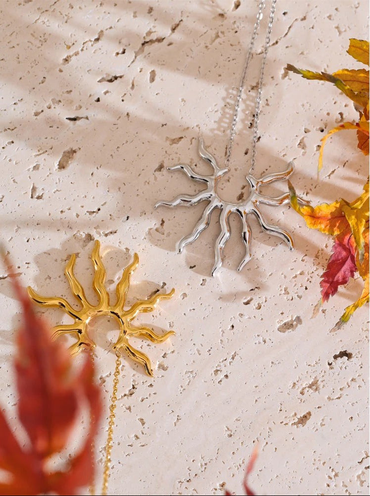 Flat lay of gold and silver wavy sun pendant necklaces on stone with fall foliage