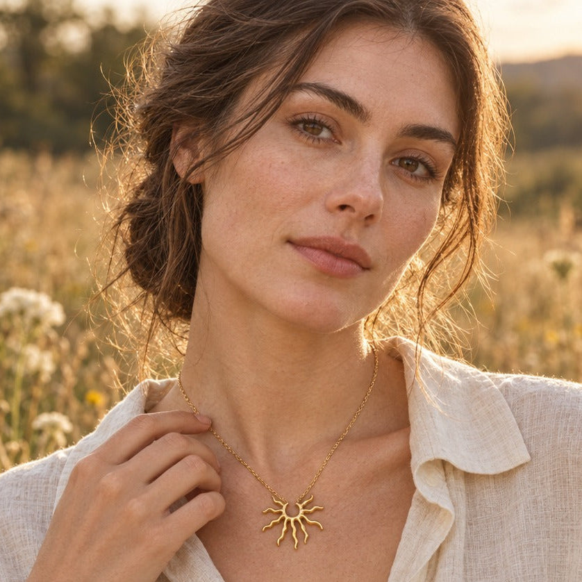 Woman in a linen shirt wearing a gold wavy sun pendant necklace in a golden-hour meadow