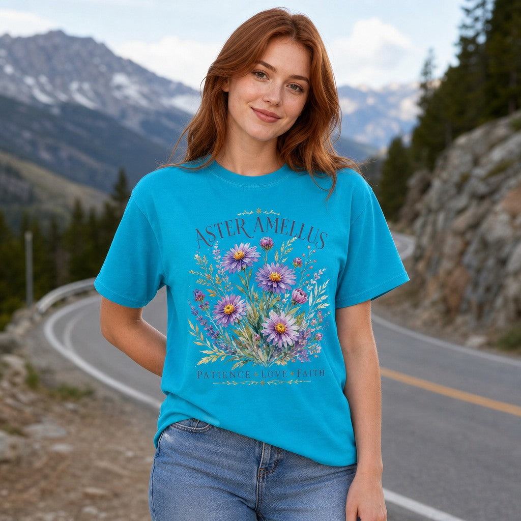 Woman in sapphire blue Comfort Colors 1717 t-shirt featuring a whimsical hand-painted watercolor bouquet of purple Aster Amellus flowers and wild botanicals, standing on a mountain road, perfect for garden lovers, nature enthusiasts, and mindful souls, by Crossroads Dandelion