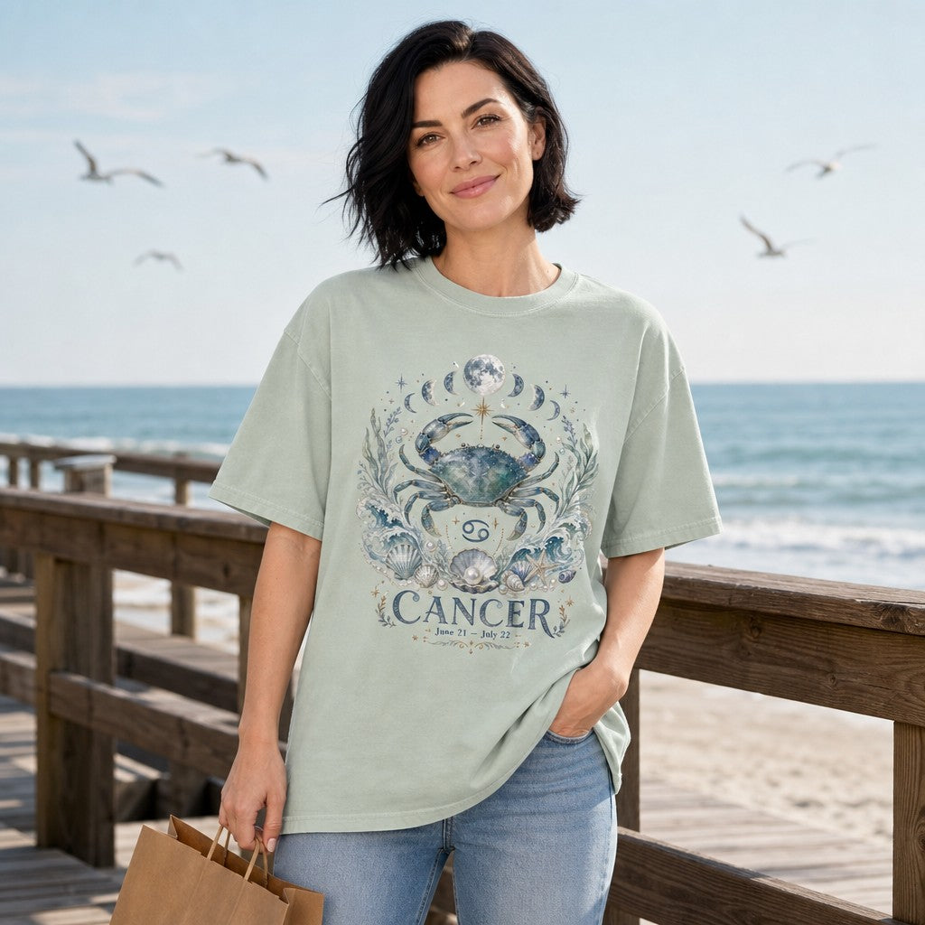 Woman on a sunny beach boardwalk wearing a Comfort Colors 1717 tee in bay, featuring a whimsical hand-painted Cancer zodiac artwork with a celestial crab, lunar phases, ocean waves, seashells, and pearls, perfect for astrology lovers and mystical water sign souls, by Crossroads Dandelion