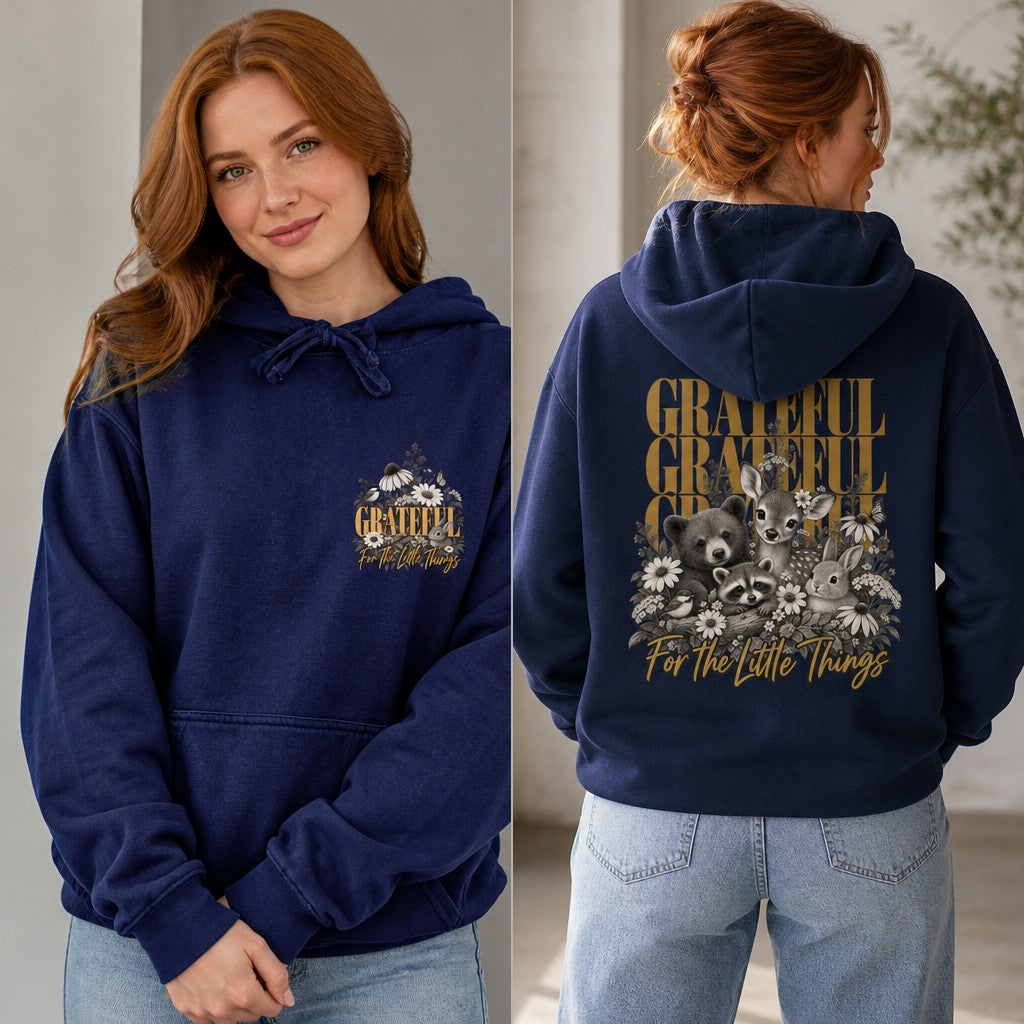 Woman wearing a true navy hoodie with a whimsical woodland animals and floral graphic, script 'Grateful for the Little Things' text, cozy indoor setting, perfect for nature lovers and women seeking cute cozy apparel, by Crossroads Dandelion