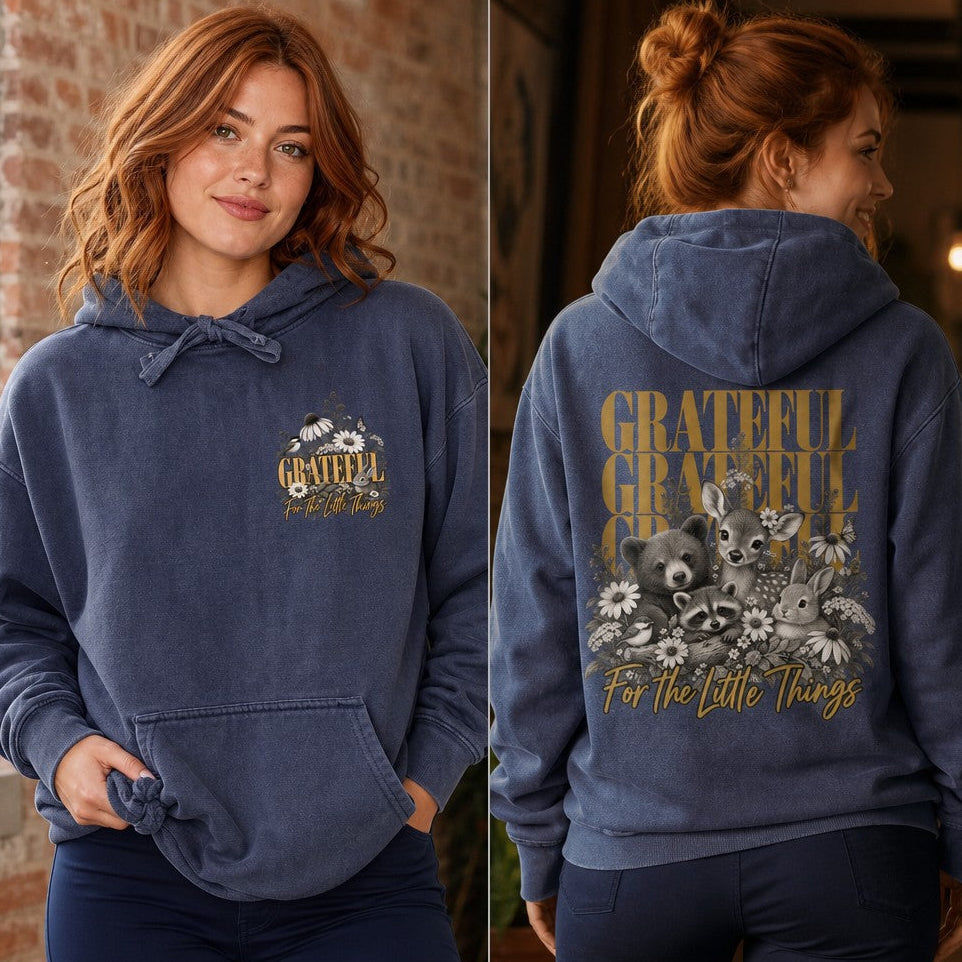 Woman wearing a denim hoodie with a whimsical 'Grateful for the Little Things' design featuring cute illustrated animals, florals, and retro text on the back and front, cozy casual indoor scene, perfect for women who love gratitude-inspired art, by Crossroads Dandelion