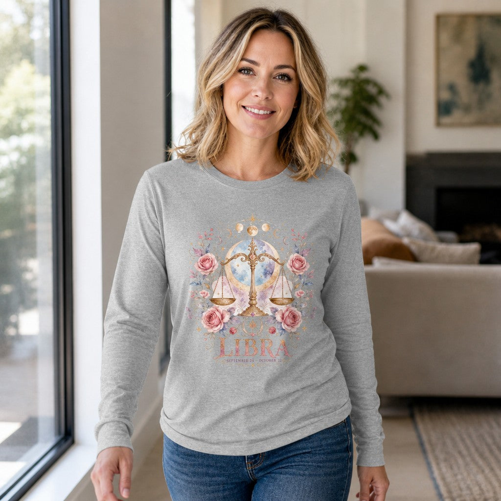 Woman in an athletic heather Bella Canvas 3501 long sleeve shirt featuring a whimsical watercolor Libra design with golden scales, pink roses, botanicals, and celestial accents, standing in a modern living room, perfect for zodiac lovers and nature art fans, by Crossroads Dandelion