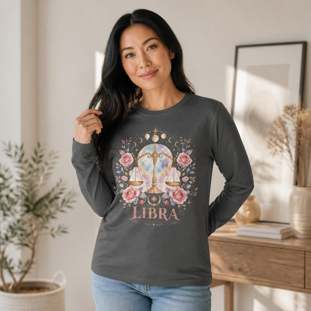 Woman wearing an asphalt Bella Canvas 3501 long sleeve shirt featuring a whimsical watercolor Libra design with golden scales, blush pink roses, celestial moon backdrop, perfect for zodiac and vintage botanical lovers, in a cozy home setting, by Crossroads Dandelion