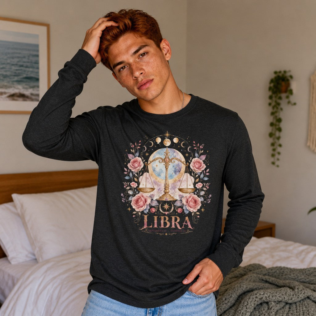 Man wearing a dark grey heather Bella Canvas 3501 long sleeve featuring a whimsical watercolor Libra scales design framed by pink roses, celestial moon backdrop, and botanicals, styled for zodiac and vintage art lovers, photographed in a cozy bedroom setting, by Crossroads Dandelion