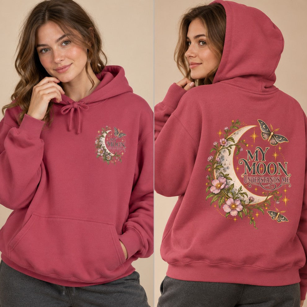 Woman wearing a crimson hoodie featuring a whimsical crescent moon with butterflies, pink flowers, sparkling stars, and the phrase 'My Moon Understands Me' on the back, cozy at home loungewear for women, dreamy fantasy design, by Crossroads Dandelion