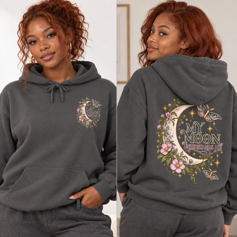 Woman in a pepper gray hoodie featuring a whimsical celestial moon, floral, and moth design with the words 'My Moon Understands Me', cozy indoor scene, perfect for women and lovers of mystical, boho, and cottagecore aesthetics, by Crossroads Dandelion