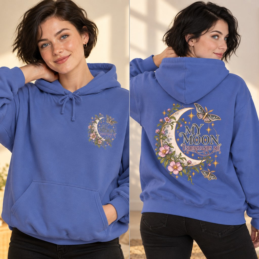 Woman in flo blue hoodie featuring a whimsical celestial and floral back design with the phrase 'My Moon Understands Me,' illustrated with flowers, butterflies, and a crescent moon, cozy indoor setting, feminine style for women and moon lovers, by Crossroads Dandelion
