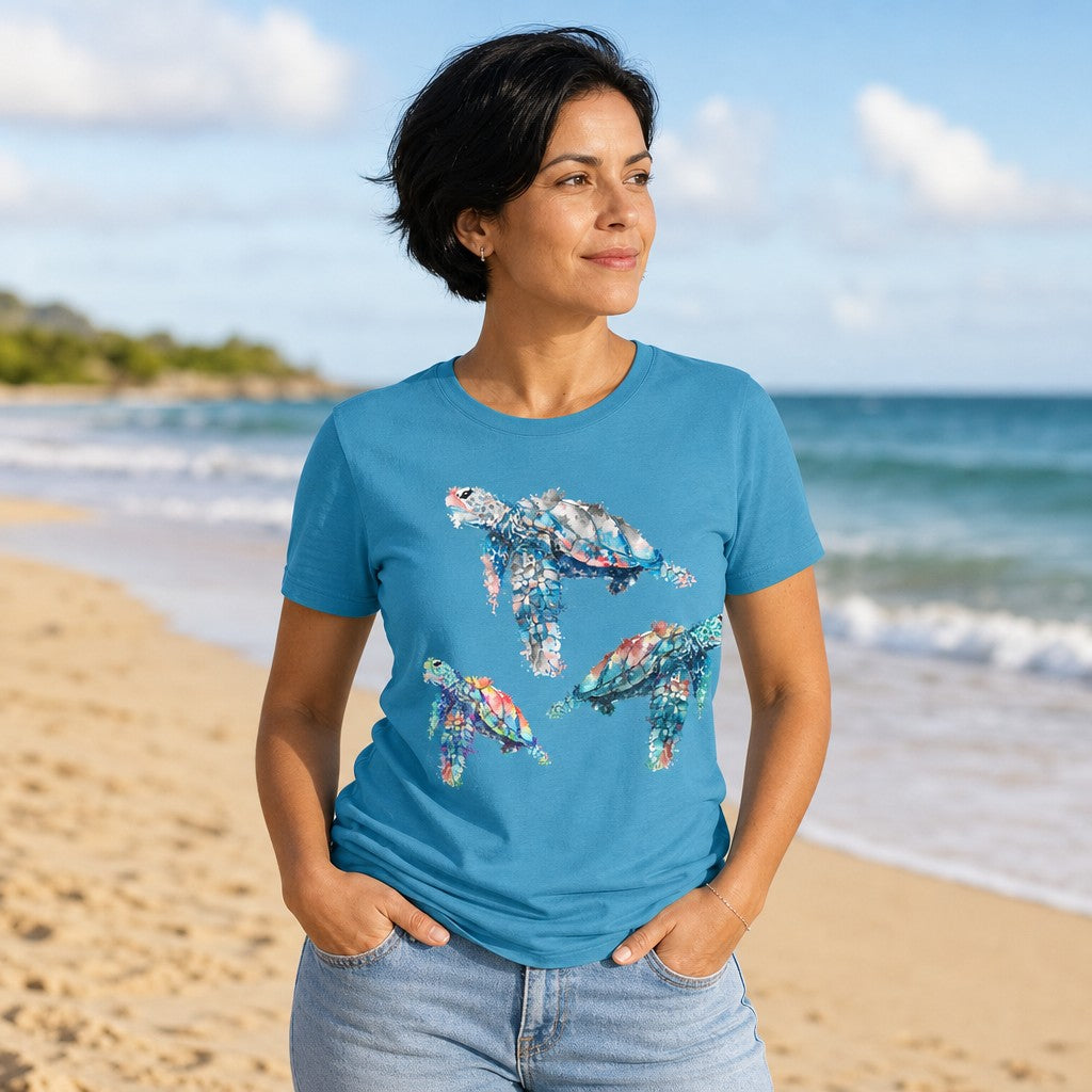 Woman wearing aqua Bella Canvas 3001 t-shirt with dreamy watercolor sea turtles illustration in blues, teals, and corals, standing on a sunny sandy beach, by Crossroads Dandelion